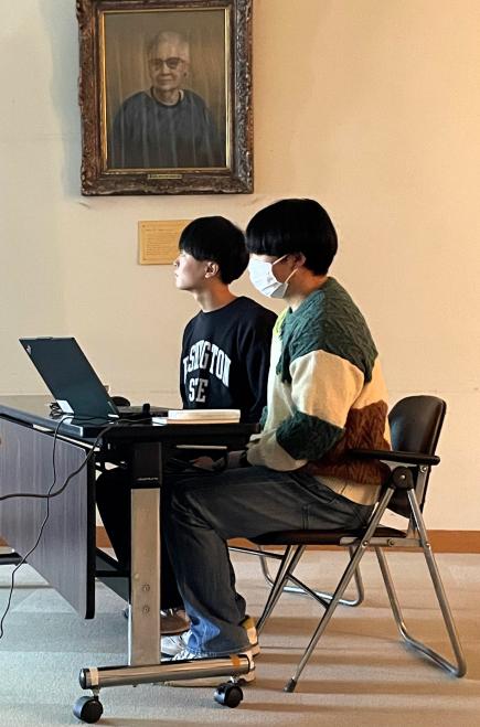 真剣な表情でプレゼンを行う学生たち。奥の肖像画はジェシー校長